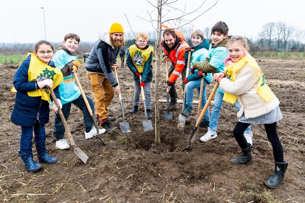 Kinderen en leden va de organisatie steken een schop in de grond en maken ruimte voor het planten van een boom